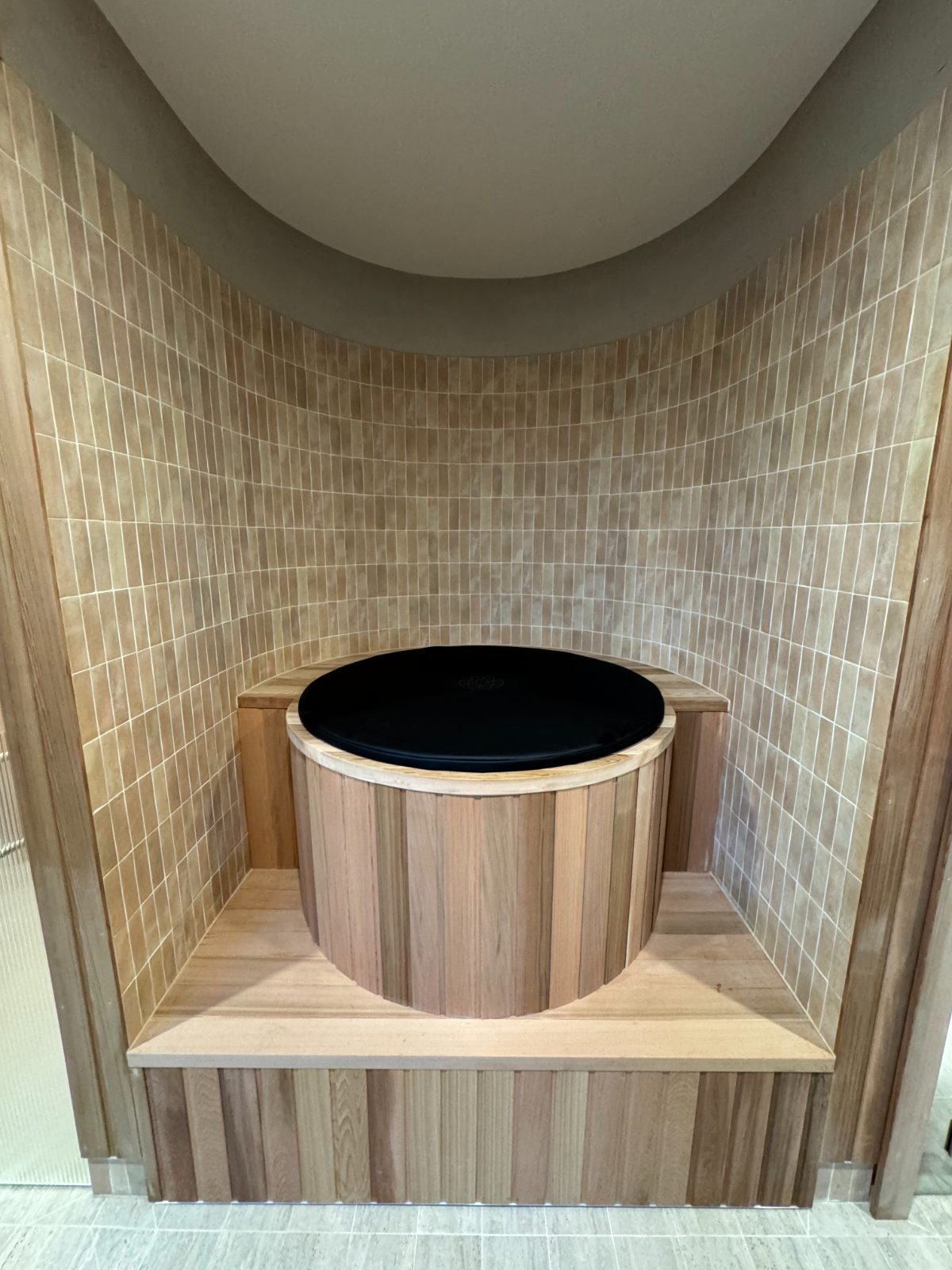 Cedar-clad round cold plunge built into a tiled alcove